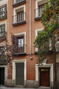 Facade of a narrow building built with exposed clay brick, balconies with wrought iron railings and a portal with a wooden door