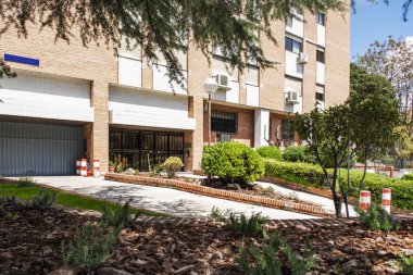 Facade of a building with gardens, trees, a black metal portal and an access ramp to the garage next to it
