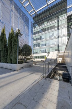 Facade of an office building with glass and metal, granite surfaces with marble stairs with metal railings and decorative trees