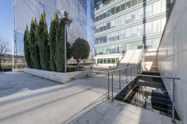 Facade of an office building with marble stairs with metal railings and decorative trees