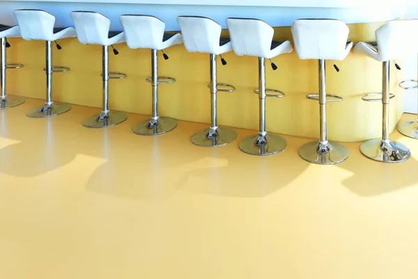 A counter with lots of metal stools with white upholstery and plain yellow floors