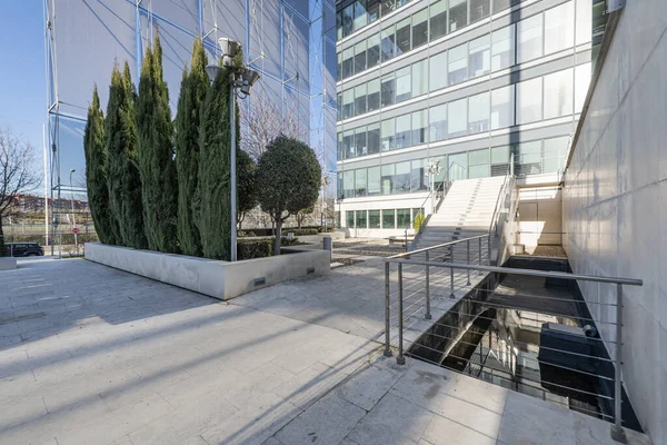 Facade of an office building with marble stairs with metal railings and decorative trees