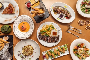 Still life of delicious dishes with Spanish recipes and salads, serrano ham croquettes, entrecote steak cooked on charcoal, fried artichoke flower and salad with goat cheese