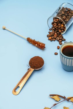 Coffee still life with beans, an espresso, a ladle with ground coffee and an individual coffee pot on a blue table