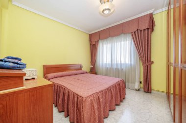 Bedroom with a double bed with a red bedspread to match the curtains and cherry wood furniture