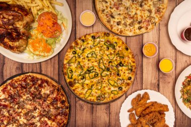 Top view image of freshly cooked pizzas in the stone oven and assorted chicken dishes