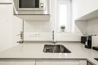 Detail of a kitchen with a gray stone worktop with a stainless steel microwave and sink