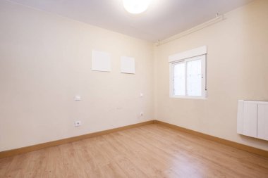 Empty room with cream colored walls with a single aluminum window with sliding panes and wooden flooring