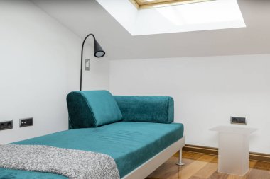 Living room of a loft-style holiday apartment with skylights in the sloping ceiling and green velvet chaise longue sofa with gray metal frame