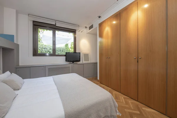 Double bedroom with a bed with a gray headboard, low gray furniture and a built-in wardrobe with oak doors