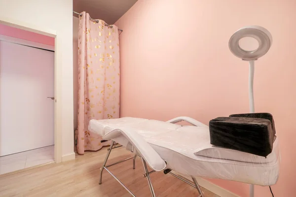 Massage booth with a folding table in a beauty salon with pink walls, a white circular lampshade and a dressing room with curtains