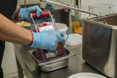 Detail of hands of a chef with blue plastic gloves grating tomato in the kitchen