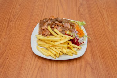 A large plate of fried potato kebab with salad and mixed chicken and lamb meat on a cherry wood table and white plate