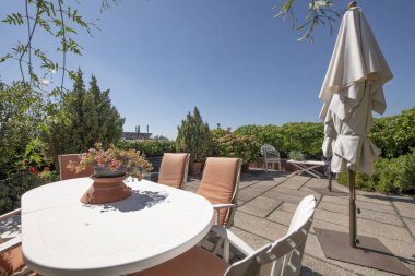 Terrace of a mansard house with vines on walls and house. Cement and stone tile floors and white cloth folding umbrellas and white resin table with matching chairs