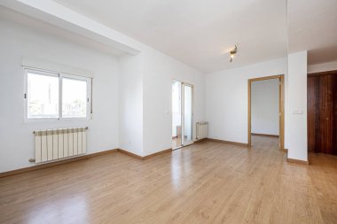Living room of an empty house with oak wooden doors, exit to a terrace with aluminum sliding doors and oak wooden flooring and several aluminum radiators