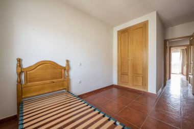 Bedroom with a built-in wardrobe with oak doors, red stoneware floors and a bed with a wooden box spring