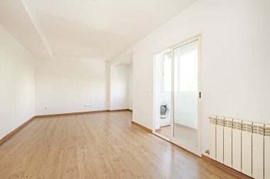 Empty living room of a home with oak laminate flooring with matching skirting boards and doors, enclosed terrace with double pane aluminum door with a washing machine inside