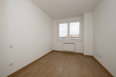Empty room with dark driftwood floors, smooth white walls, and a double-paned window with a view of the city