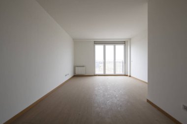 Empty room with light wooden floors, white aluminum radiators, plain white painted walls and a balcony with three aluminum and glass doors with a view
