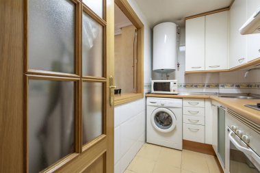 Corner kitchen with white furniture, hatch window to the living room, white appliances and electric hot water heater