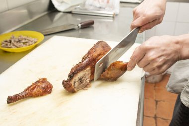 An asian chef carving a roast duck with a machete on a white teflon board