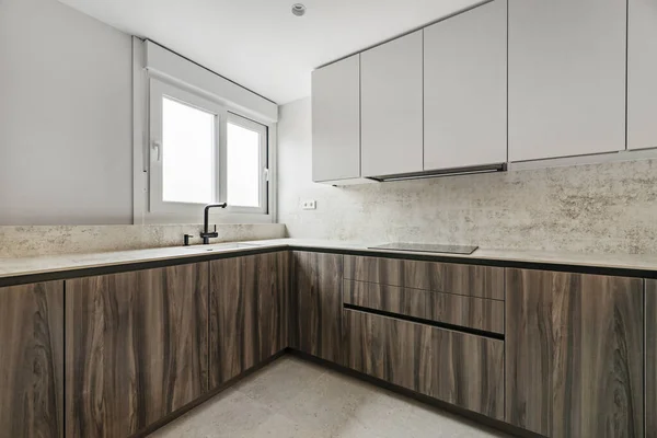 Corner of a contemporary design kitchen making a corner with high gray furniture and low root wood furniture with beige marble countertops and walls