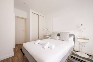Bedroom with a gray fabric double bed and white duvet with clean rolled towels and a built-in wardrobe with white wooden sliding doors