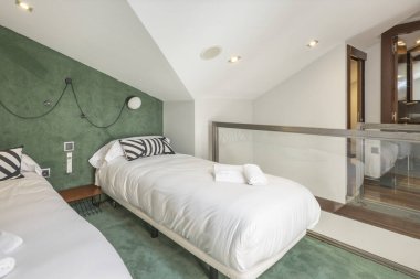 Bedroom with single beds with white duvet, green carpeted floors and hipped ceilings in a loft