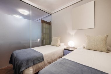 Bedroom with two single beds with white bedspreads, blue blankets and a glass partition