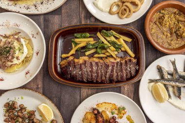 Set of dishes and tapas of Spanish gastronomy with sliced grilled beef entrecote with french fries, Galician octopus, fried anchovies, fried calamari, rice with partridge