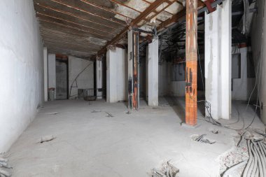 Interior premises under construction with raw cement floors and half finished electrical pipes with metal combined pillars