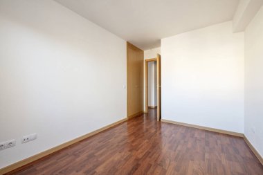 Empty room with a built-in wardrobe next to the access door, both made of oak wood to match the skirting