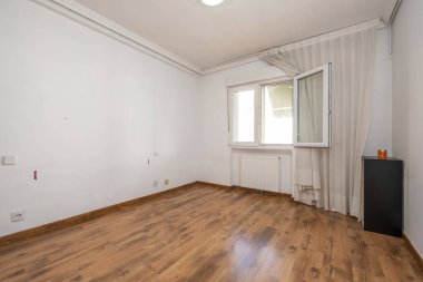 Empty room with wooden floor, plaster moldings on the ceiling, aluminum radiator, gray ceiling light, with an open double-paned window and matching skirting board