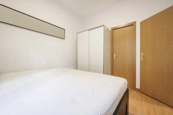 Bedroom with double bed with mattress without bedding, wardrobe with white sliding doors and oak access doors