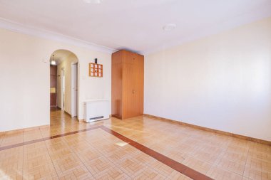 Empty living room with tiled floors and smooth soft yellow walls with an electric heater next to a solitary cupboard in one corner