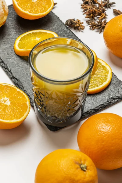 A cut glass tumbler filled with fresh orange juice surrounded by slices and whole oranges