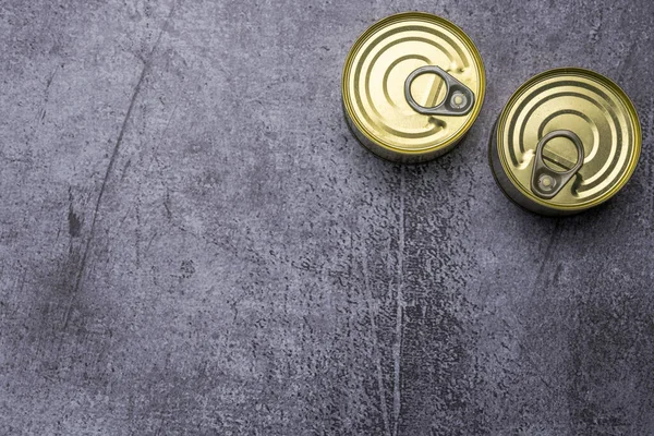 Two small circular tin cans closed with easy-open rings on gray surface