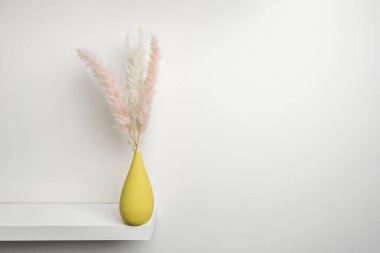 Lonely white shelf with a small yellow porcelain vase with dried decorative plants