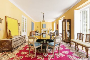 Living room of a house with ornate decoration in an eclectic style with a large Persian rug and many balconies facing the street with white wooden shutters