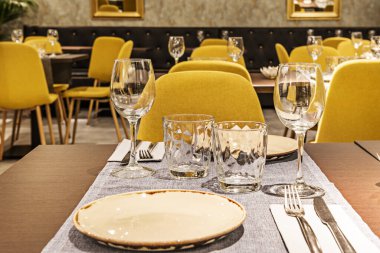 Tables in the dining room of a restaurant with service set up with porcelain tableware and glasses and glass cups