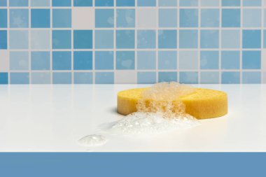 Yellow synthetic shower sponge on a white surface of a bath with foam