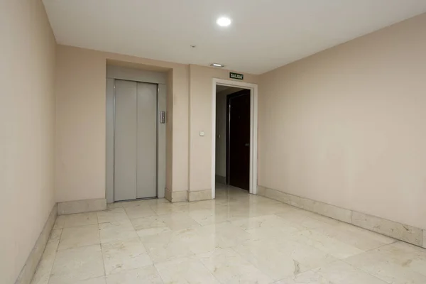 Interior of a residential housing portal with elevator with gray metal doors and polished cream marble floors