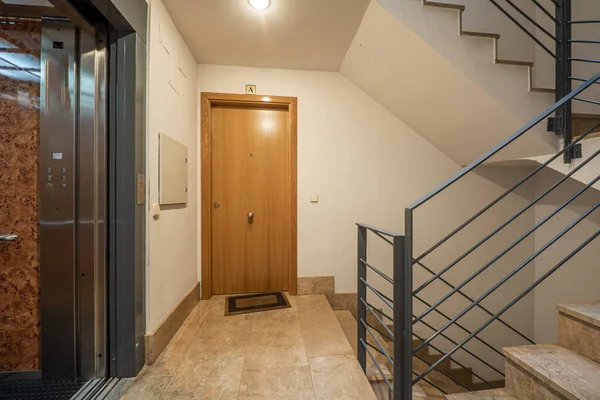 Interior of a residential apartment portal with an elevator with gray metal doors and polished cream marble floors, gray metal railings and marble stairs
