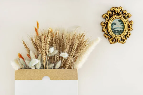 A cardboard bag with decorative dried vegetable pods and buckwheat ears next to a gilded wooden frame
