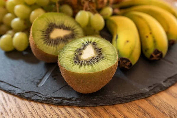 A black slate fruit tray with kiwis in the foreground