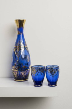 A transparent blue glass bottle with gold decorations and glasses of the same set