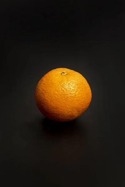 A lone orange with its rough skin on a black surface