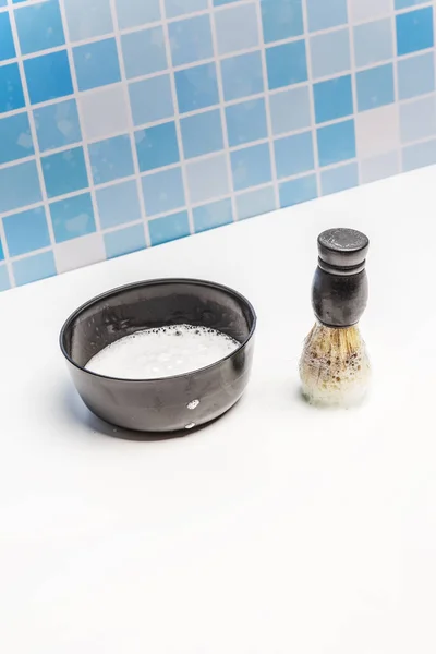 A black container with foam soap and a barber brush to apply foam to the face