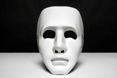 An expressionless mask of white color on a smooth white surface and black background