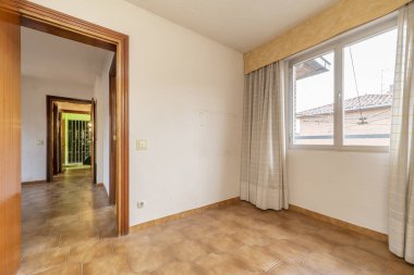 Empty room with brown stoneware floors, window with curtains and access door to other rooms